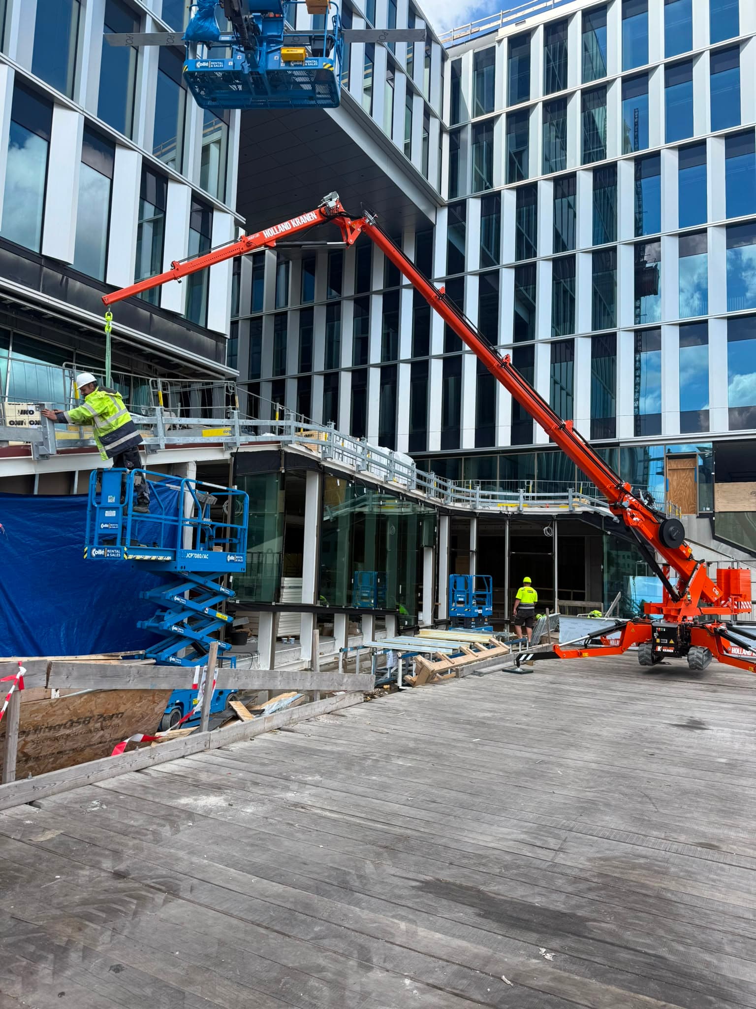 Minikraan hijst constructiemateriaal over glazen passage van kantoorgebouw