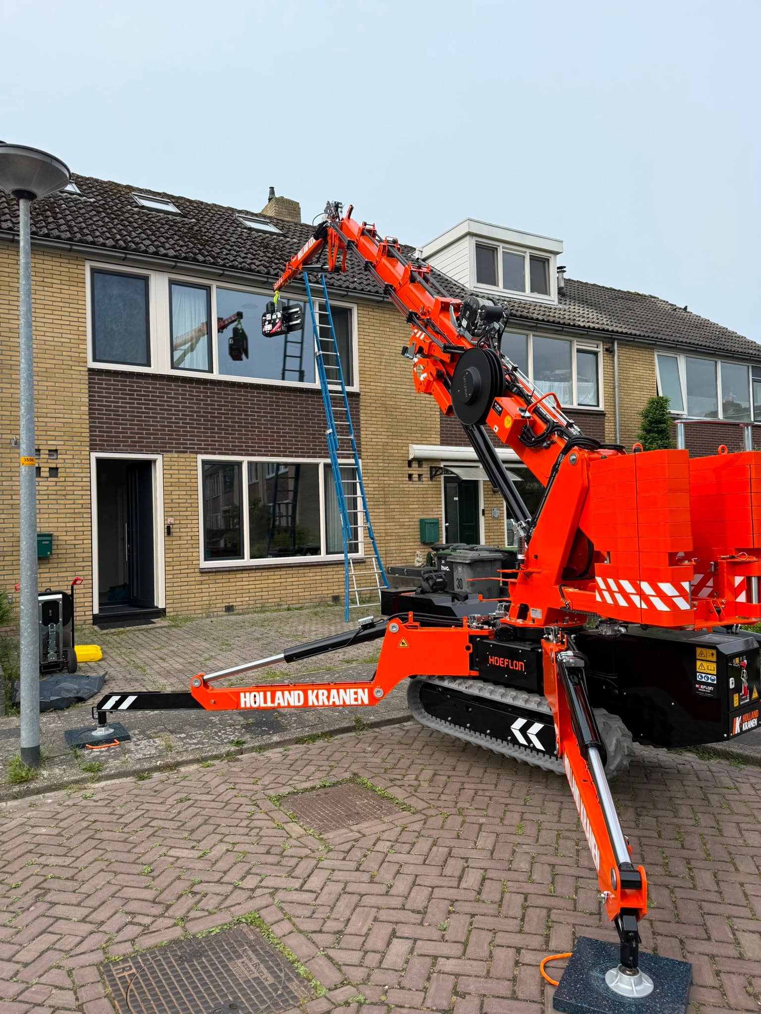 Volledig uitgeklapte minikraan hijst last naar dakraam van rijtjeswoning