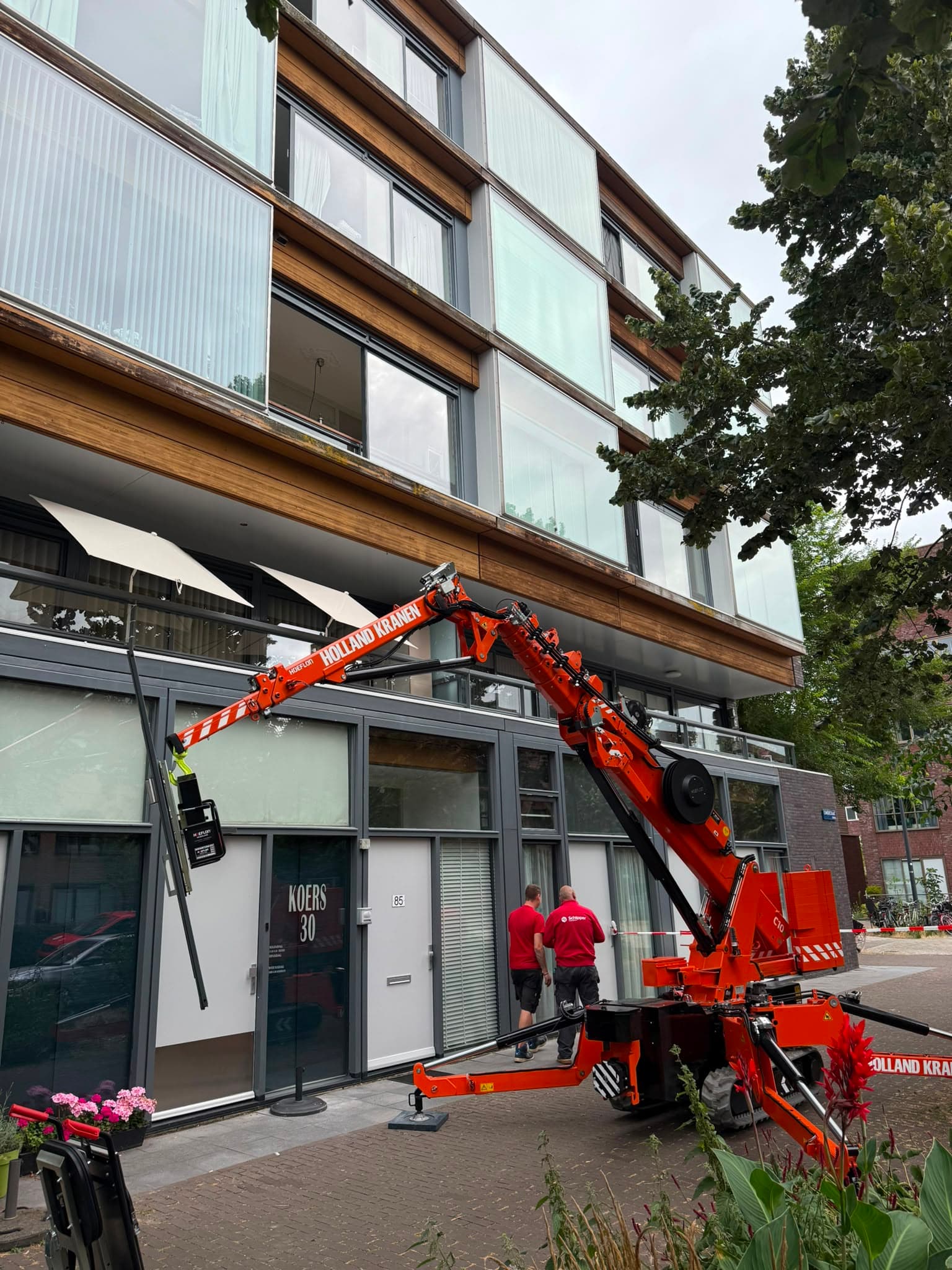 Hoeflon C10 minikraan plaatst een glaspaneel in de gevel van een appartement