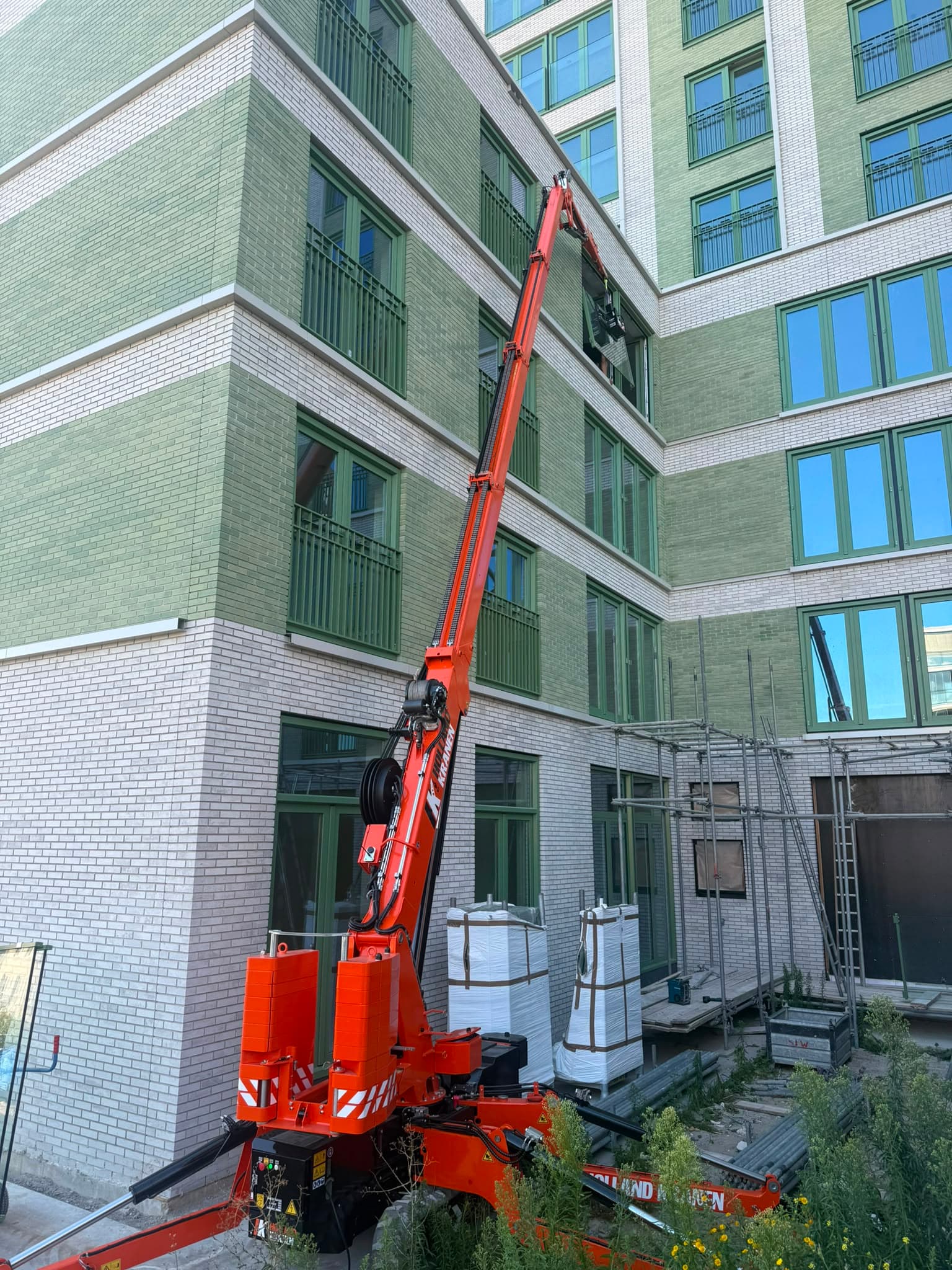 Minikraan reikt met de giek naar een gevelopening op de verdieping van een nieuwbouwpand