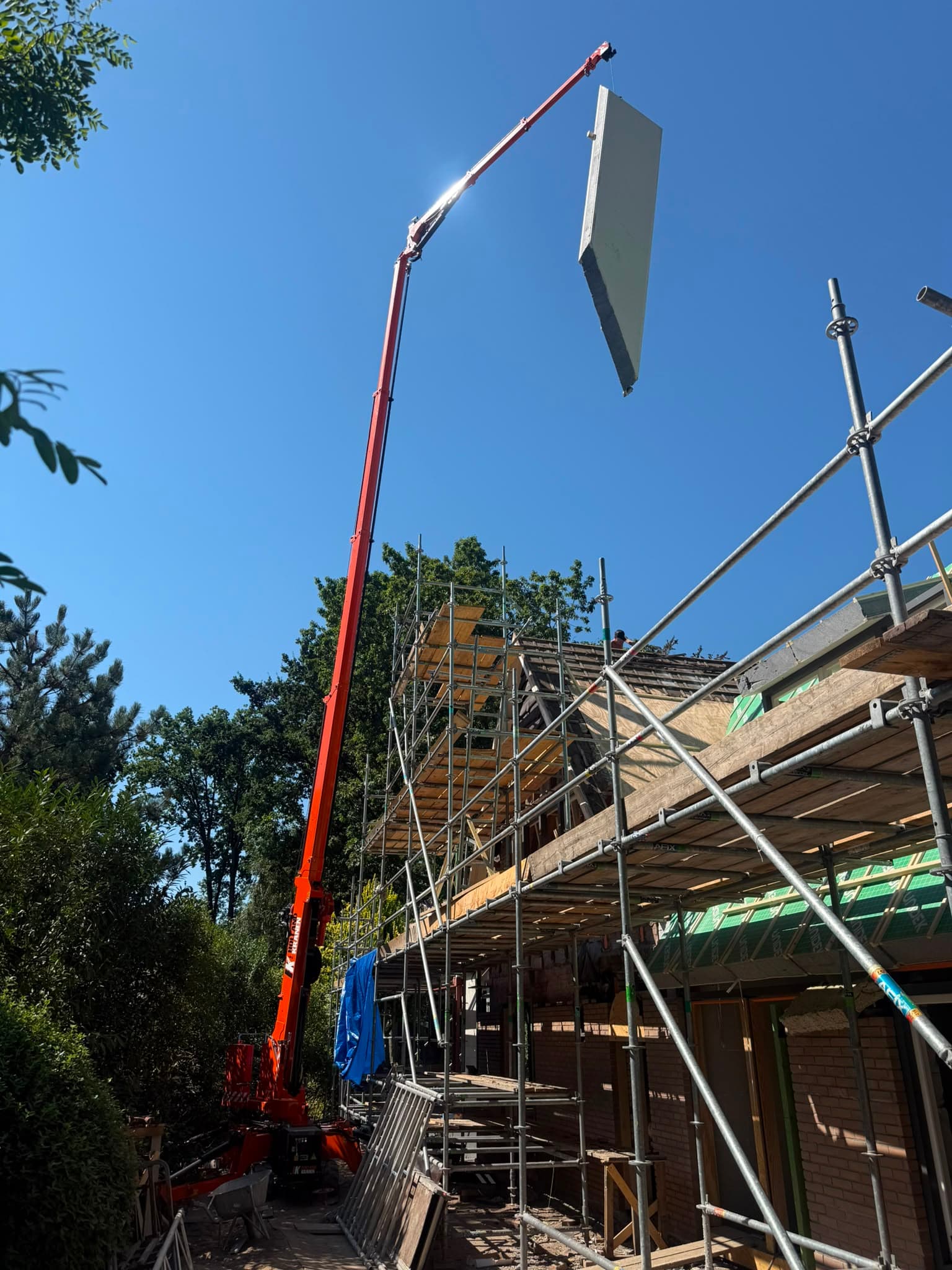 Dakelement hangt hoog aan de giek van de minihijskraan boven de steiger