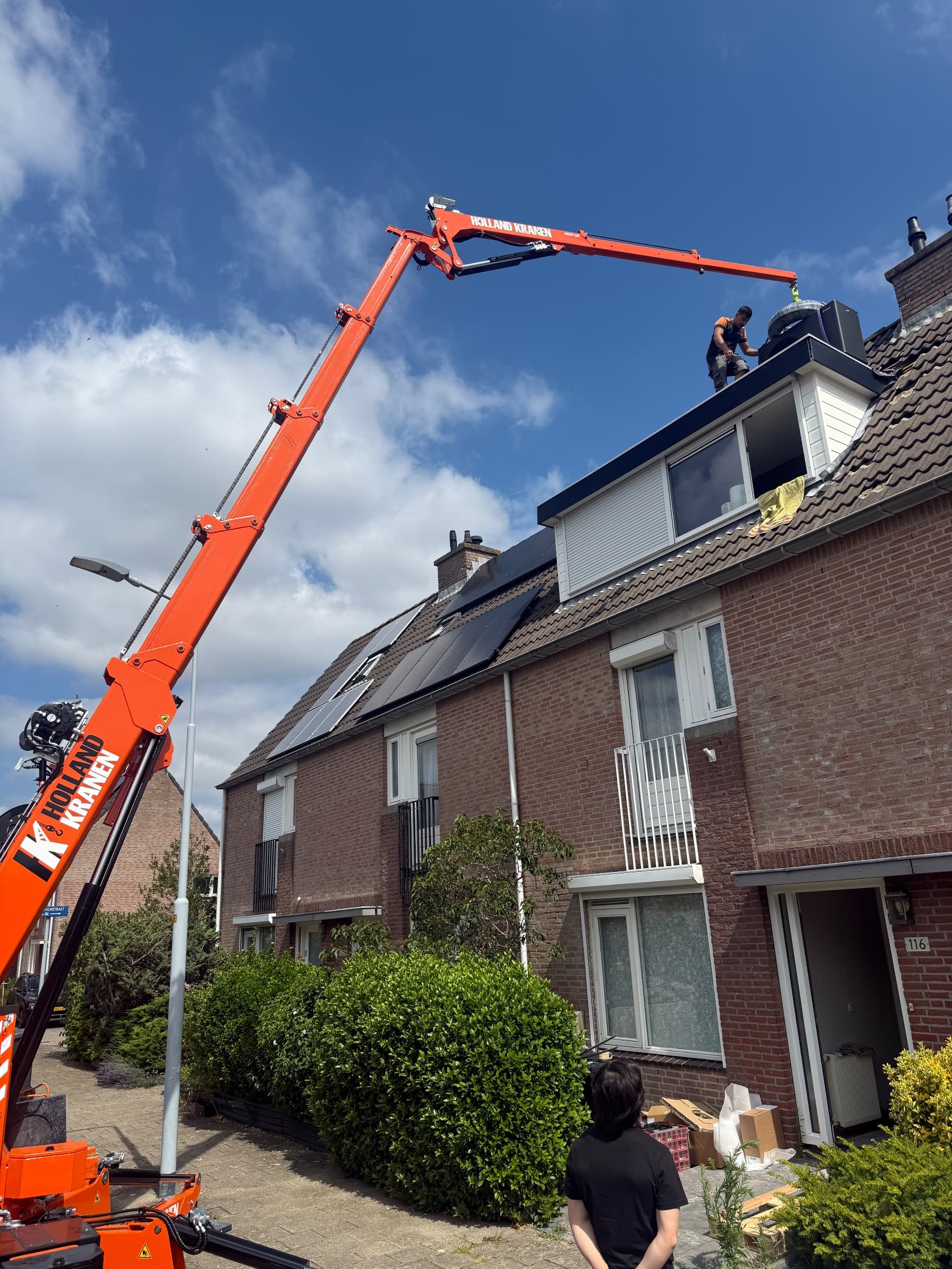 Monteur neemt de buitenunit van een warmtepomp aan op het dak van een dakkapel